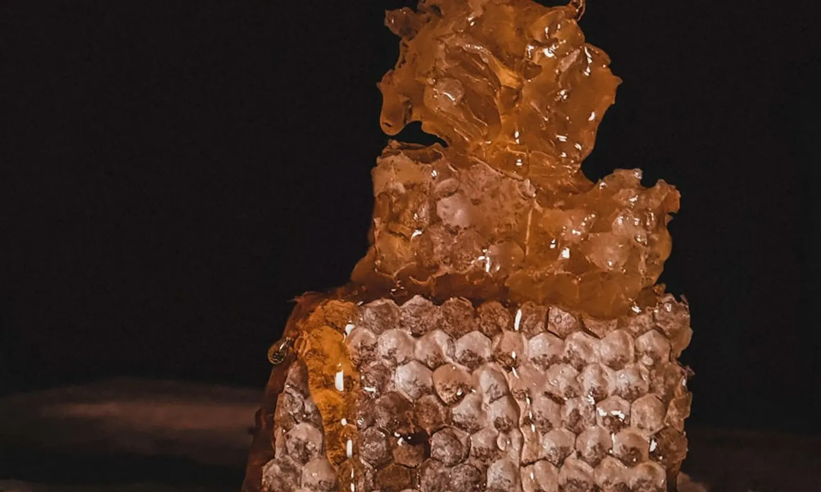 Three jars of Buzzed Honey on a stone surface, lit warmly from one side